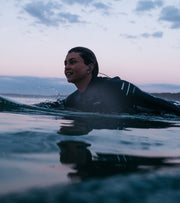 Leo on a surfboard in glassy water in evening purple light