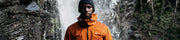 man wearing finisterre coat next to waterfall